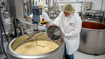 Dairy workers adding ingredients to a stainless steel processing vat in a creamery