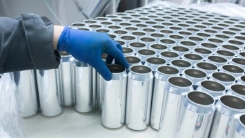 Worker handling empty aluminium containers on a dairy packaging line